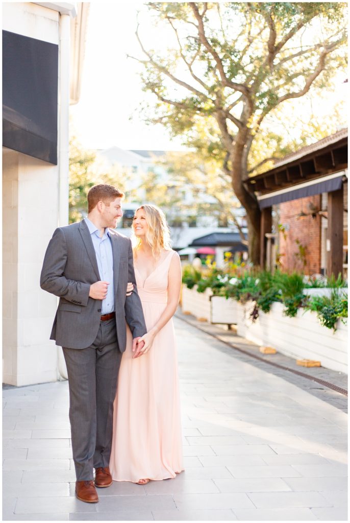 Engaged couple looks lovingly at one another in grey suit and blush dress.