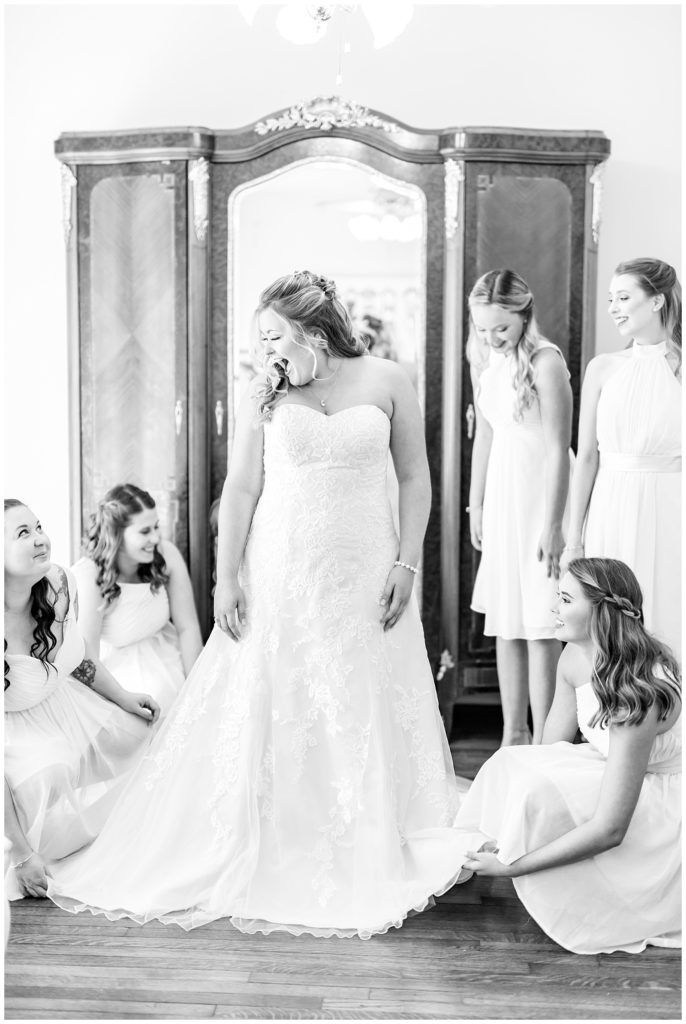 Black and white image of bridesmaids fluffing bride's wedding gown and helping her get ready the morning of her wedding day