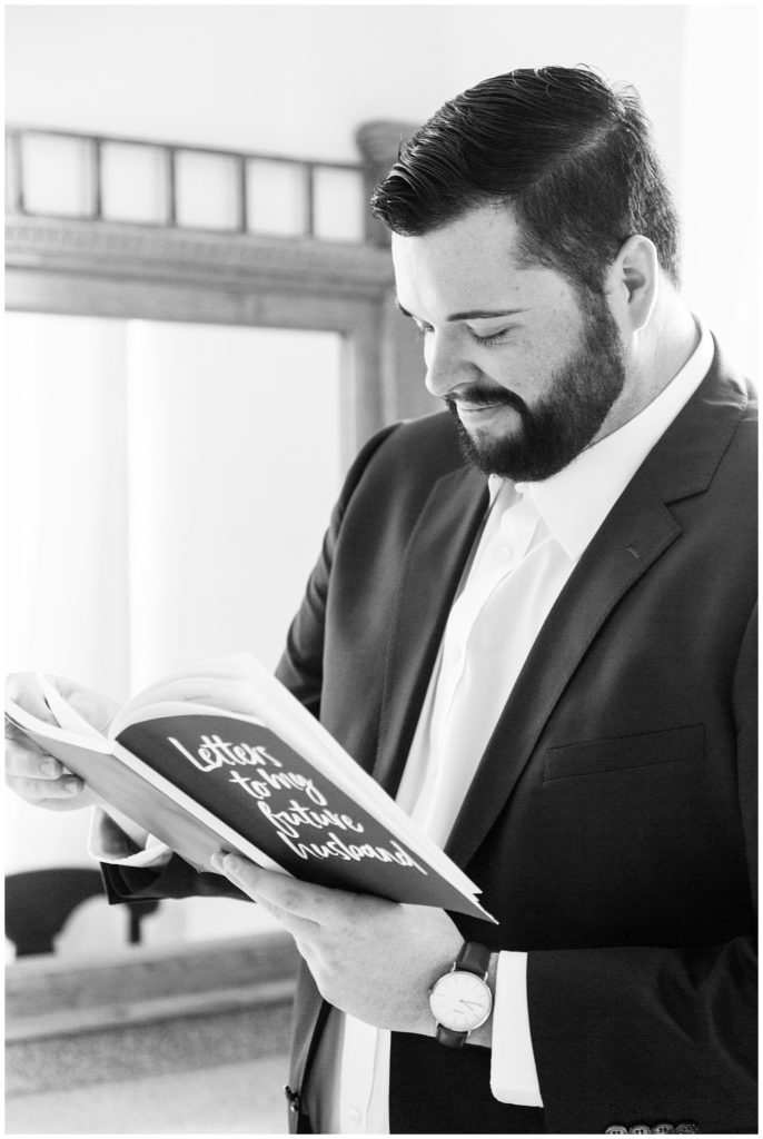 Black and white photo of groom reading a letter from his bride on their wedding day