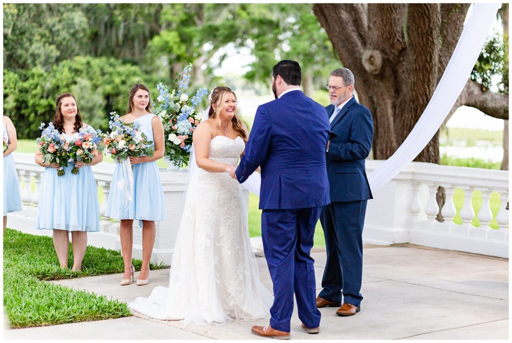 Image of bride and groom sharing a laugh during the ceremony as bridesmaids are in the background in their sky blue dresses