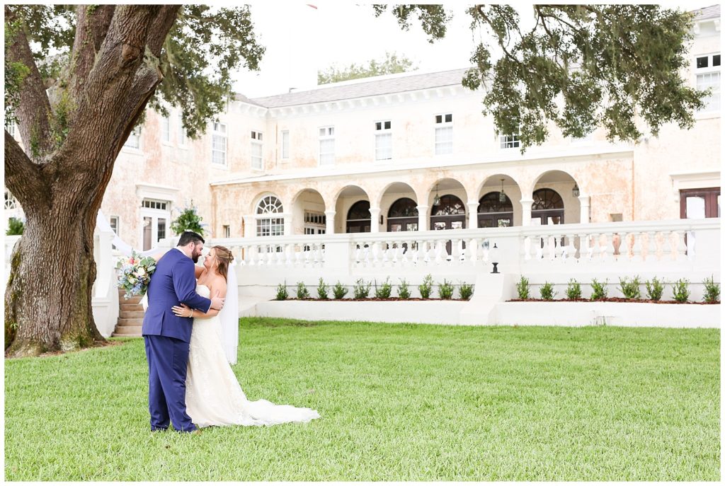 Photo of bride and groom in grassy field in front of their wedding venue, Bella Cosa Lakeside in Lake Wales Florida