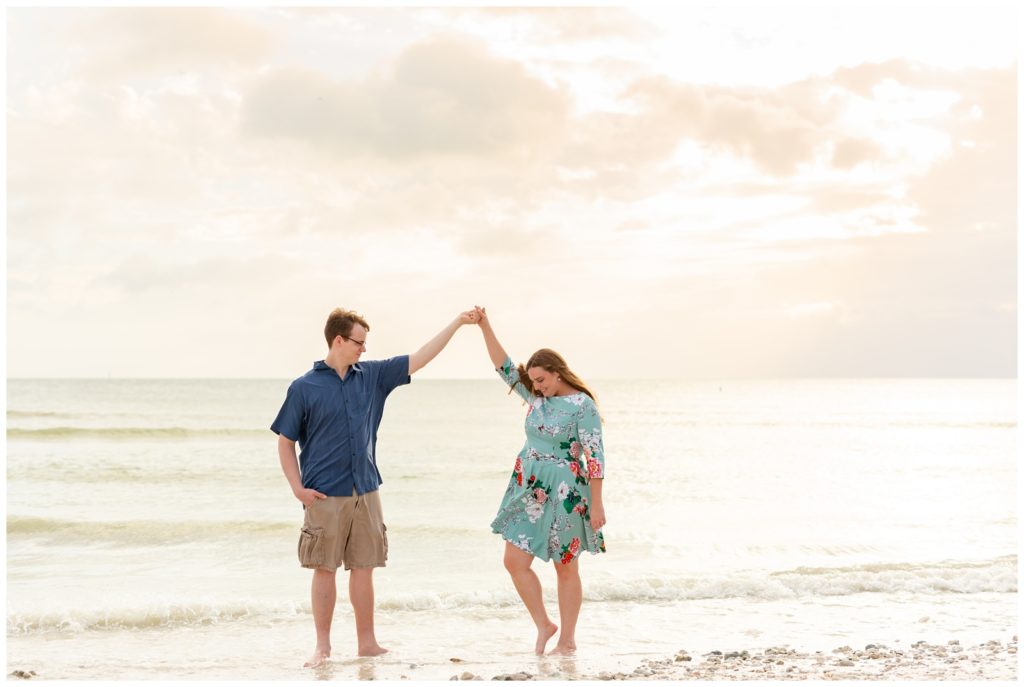Future wife twirling in the sand as fiancé holds her hand up high on the beach as the water just touches their feet in Dunedin Florida