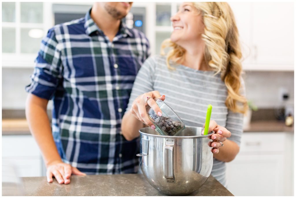 DIY couple smiling at one another in white kitchen while pouring chocolate chips into a bowl.