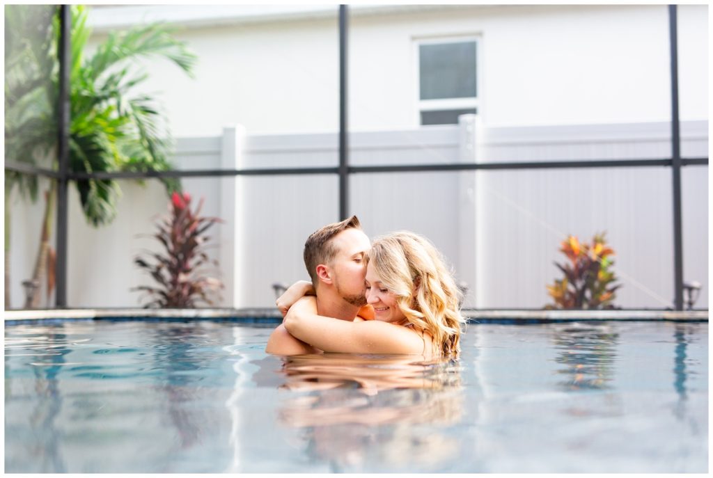 Photo of DIY couple in a pool with husband kissing his wife on the temple and wife has hands wrapped around husbands neck in Tampa Florida