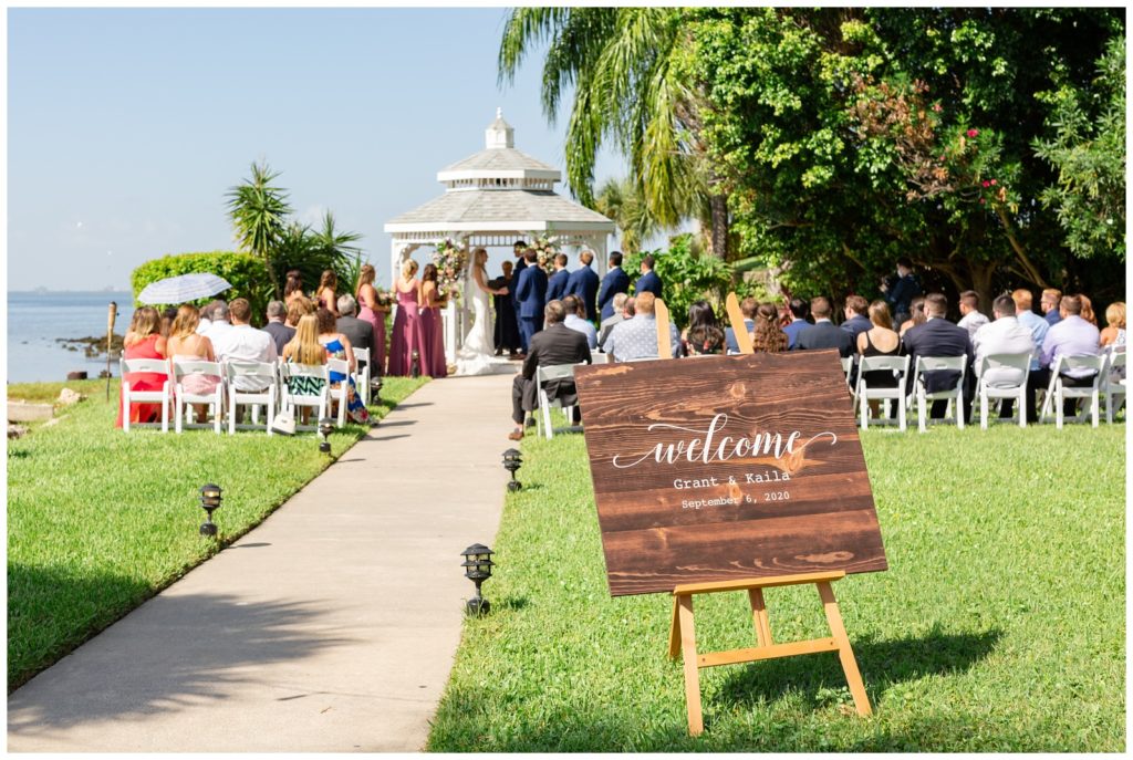 Wedding ceremony in an outside gazebo with white chairs and a "Welcome" sign at the Rusty Pelican in Tampa Florida