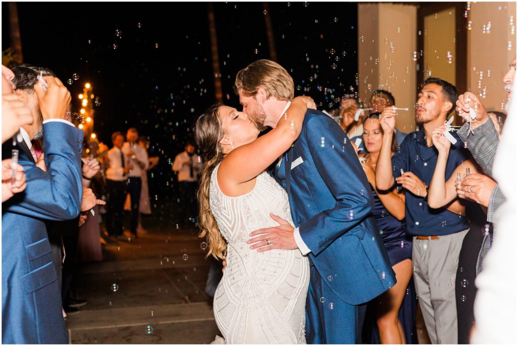 Couple sharing kiss during the exit from wedding reception with all guests blowing bubbles as a send off